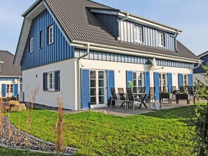 Ein zweistöckiges Haus mit einem Balkon, einer Terrasse und Gartenmöbeln sowie einem gepflegten Rasen.