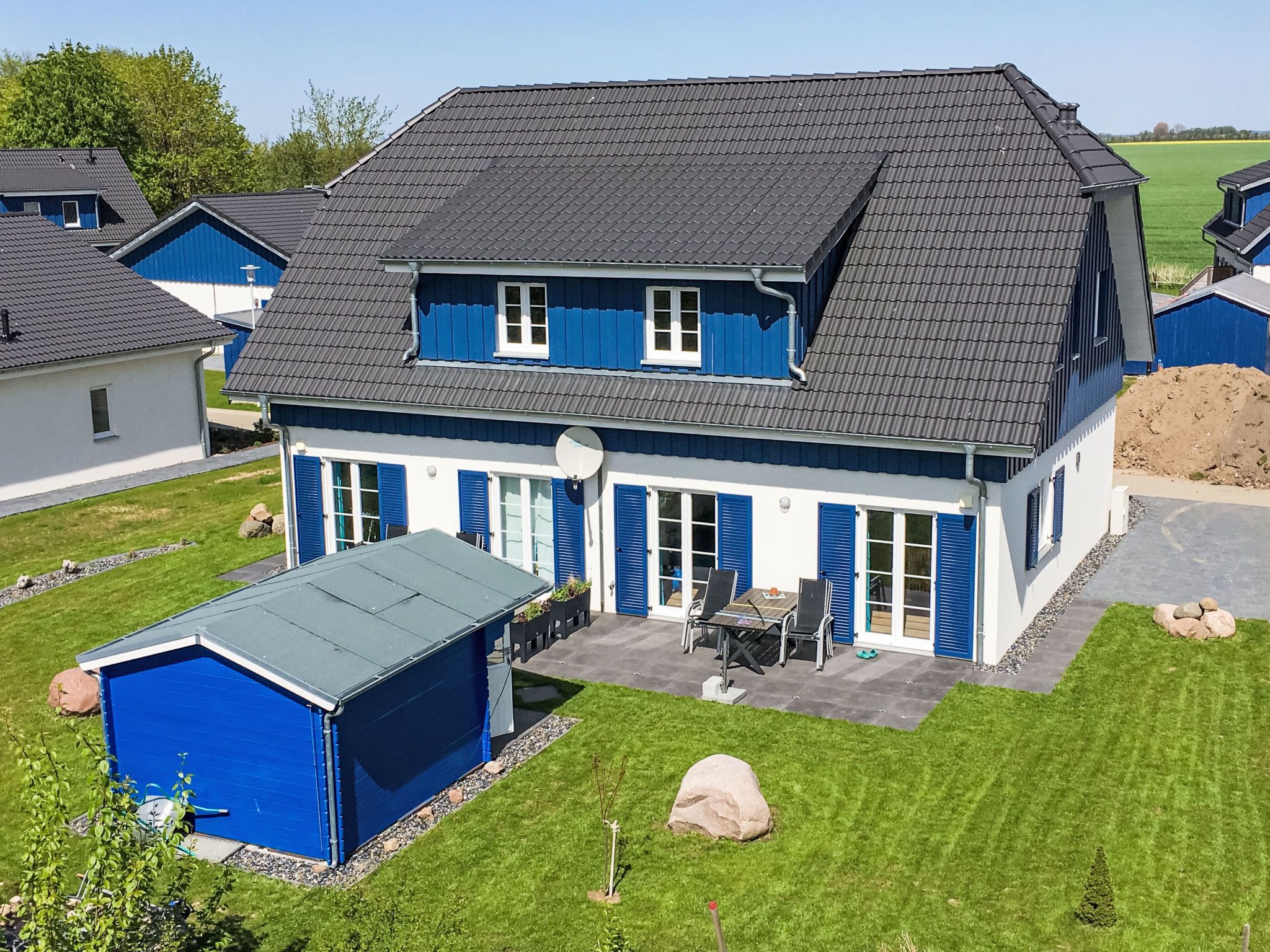 A two-story house with a dark roof, blue shutters, and a covered patio area.