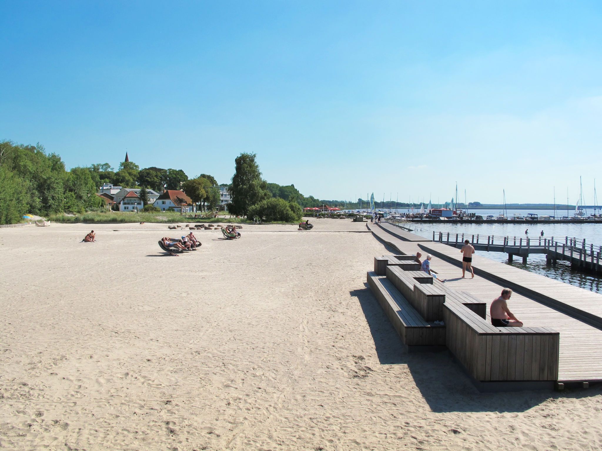 Une plage de sable avec des bancs en bois et une jetée en bois qui s’avance dans l’eau.