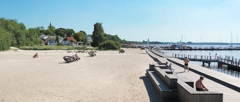 Une plage de sable avec des bancs en bois et une jetée en bois qui s’avance dans l’eau.