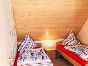 Ein kleines, gemütliches Schlafzimmer mit zwei Einzelbetten, einem Nachttisch mit Lampe und Holzboden.