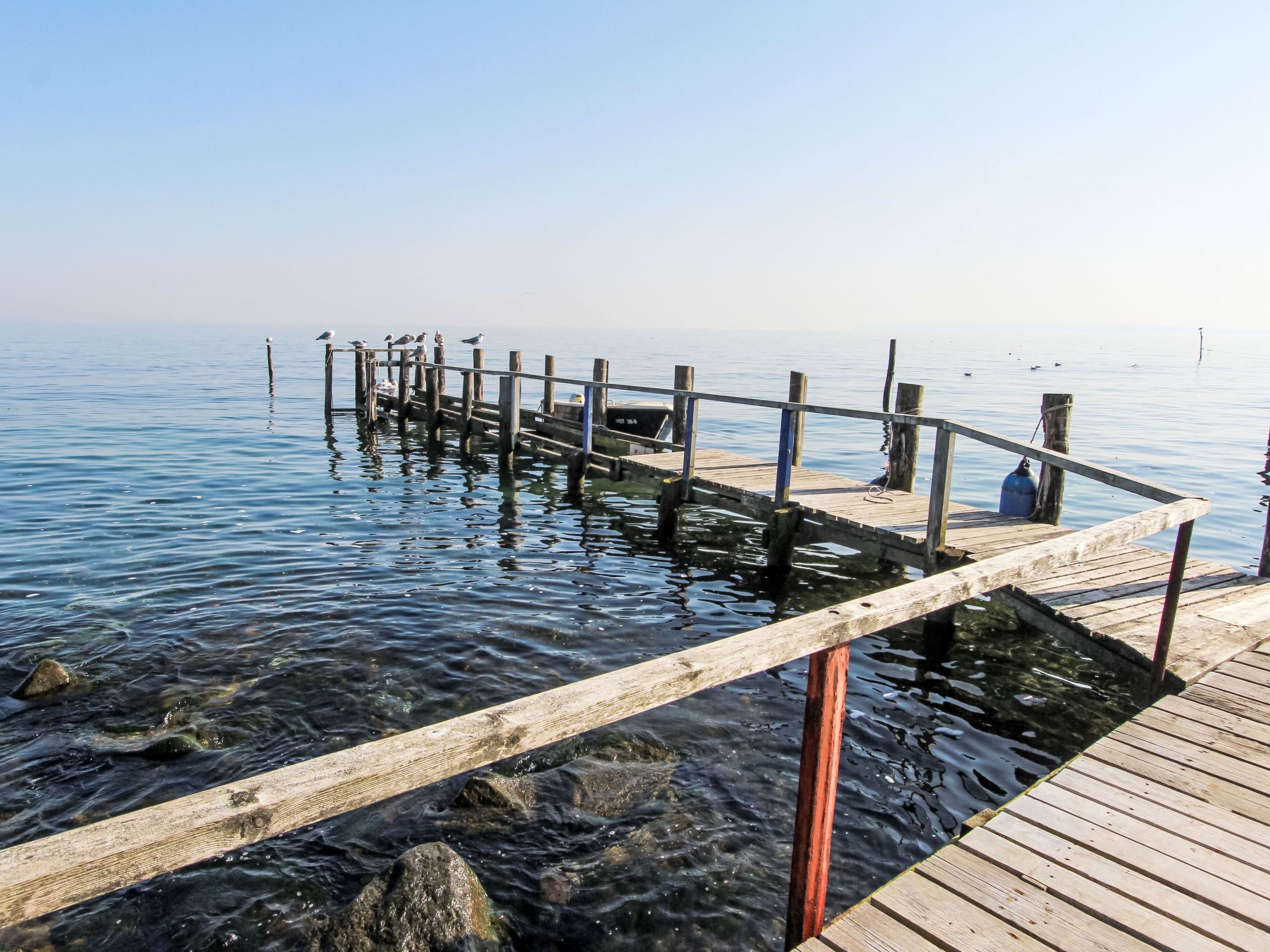Une jetée en bois s’étendant sur une étendue d’eau calme, sous un ciel dégagé.