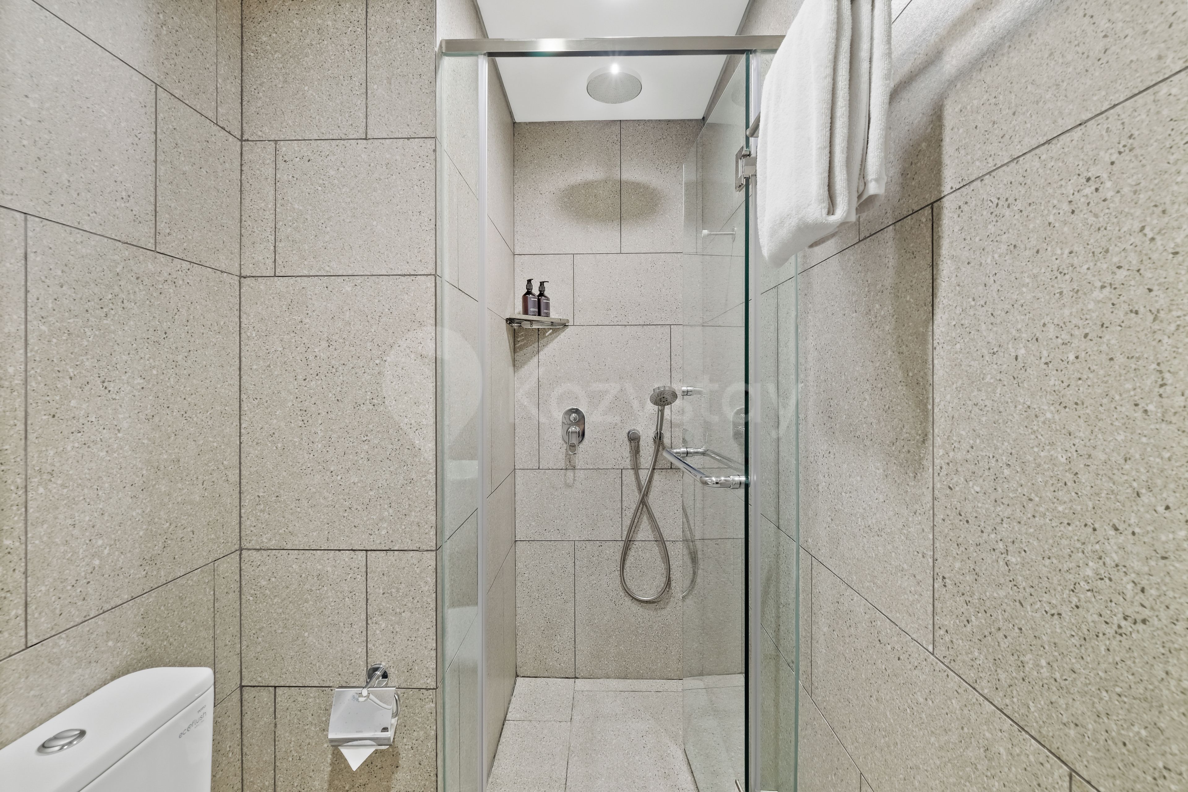 A modern bathroom with a glass-enclosed shower, a white toilet, and a shelf with toiletries.