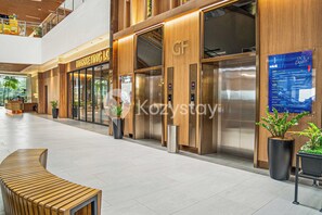 A modern hotel lobby with a wooden reception desk, a glass elevator, and a sign for 'Marketing Lo'. - Cavorel by Kozystay - Cilandak (South Jakarta)