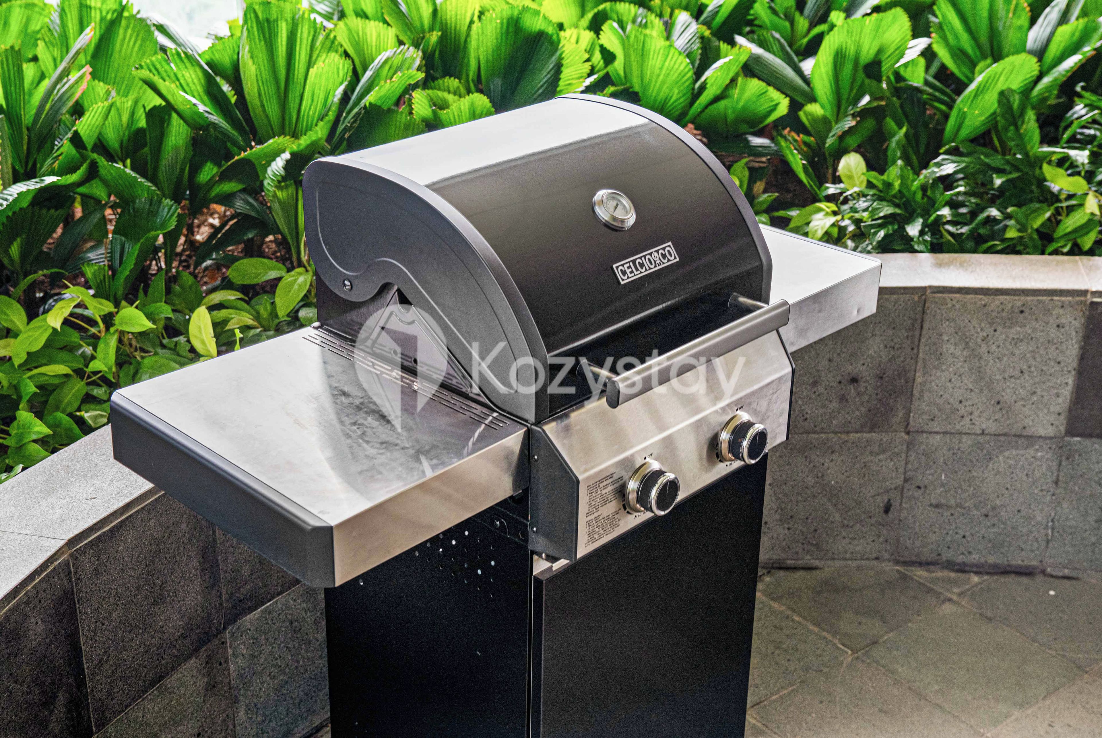 Una parrilla a gas con pantalla digital, frente a un fondo de follaje verde exuberante.