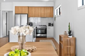 A modern kitchen with wooden cabinets, stainless steel appliances, and a dining area with a wooden table and a vase of flowers. - 15A Strangways Avenue, Hayborough Pet Friendly & Linen Included (Hayborough)