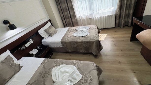 Hotellihuone, jossa on kaksi sänkyä, yöpöytä lampun kanssa, puhelin ja ikkuna, jossa on verhot.