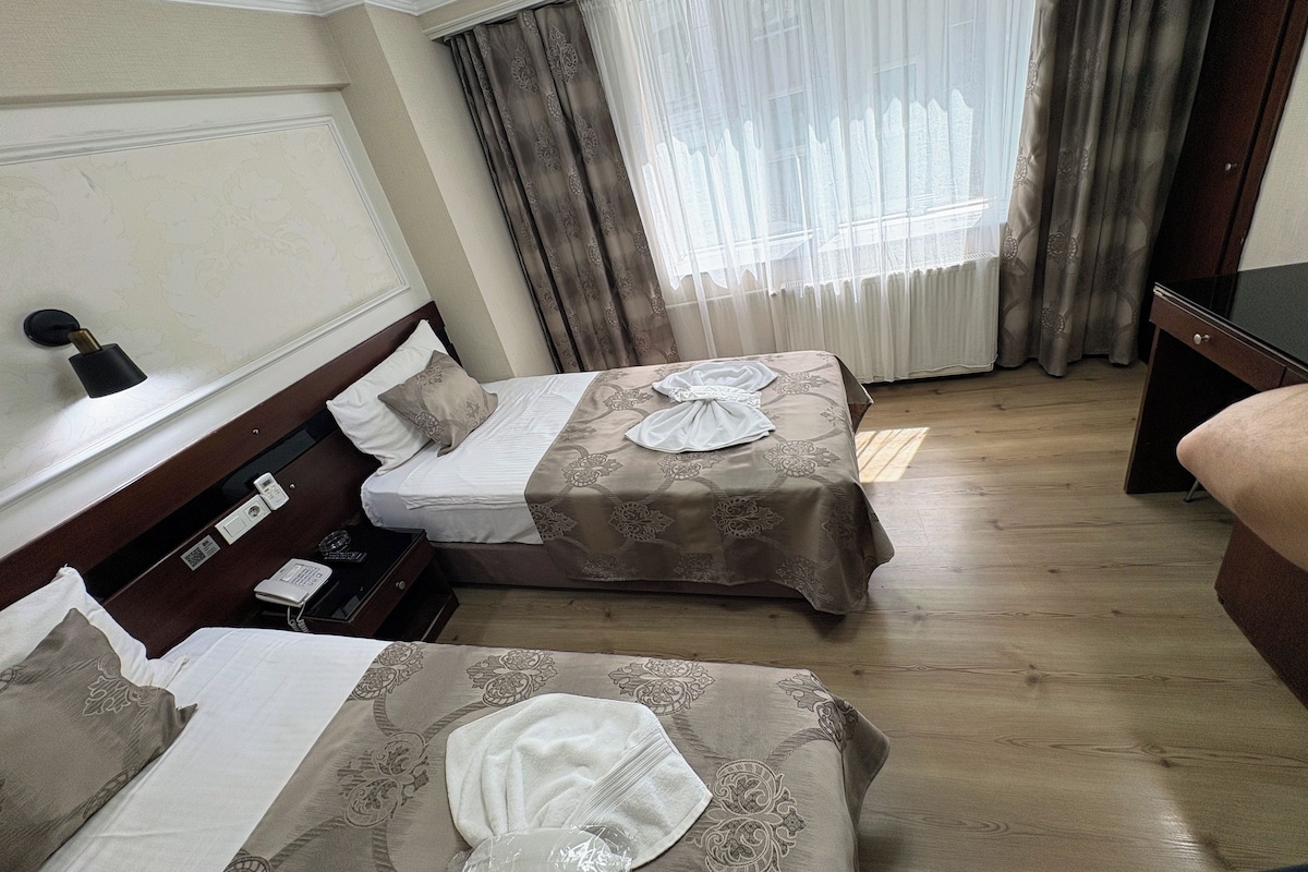 Une chambre d’hôtel avec deux lits, une table de chevet avec une lampe, un téléphone et une fenêtre avec des rideaux.