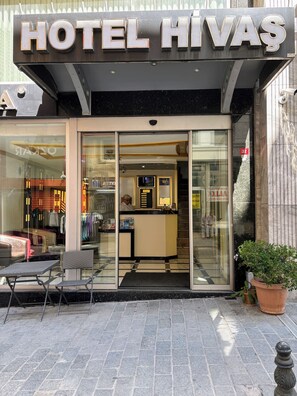 A hotel entrance with a glass door, a reception desk, and a seating area outside. - Hivaş hotel (Istanbul)
