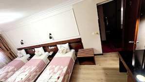 Hotellihuone, jossa on kaksi sänkyä, puinen pääty, pieni pöytä ja vaatekaappi.