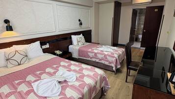 A hotel room with two beds, a desk, a mirror, and a bathroom door.