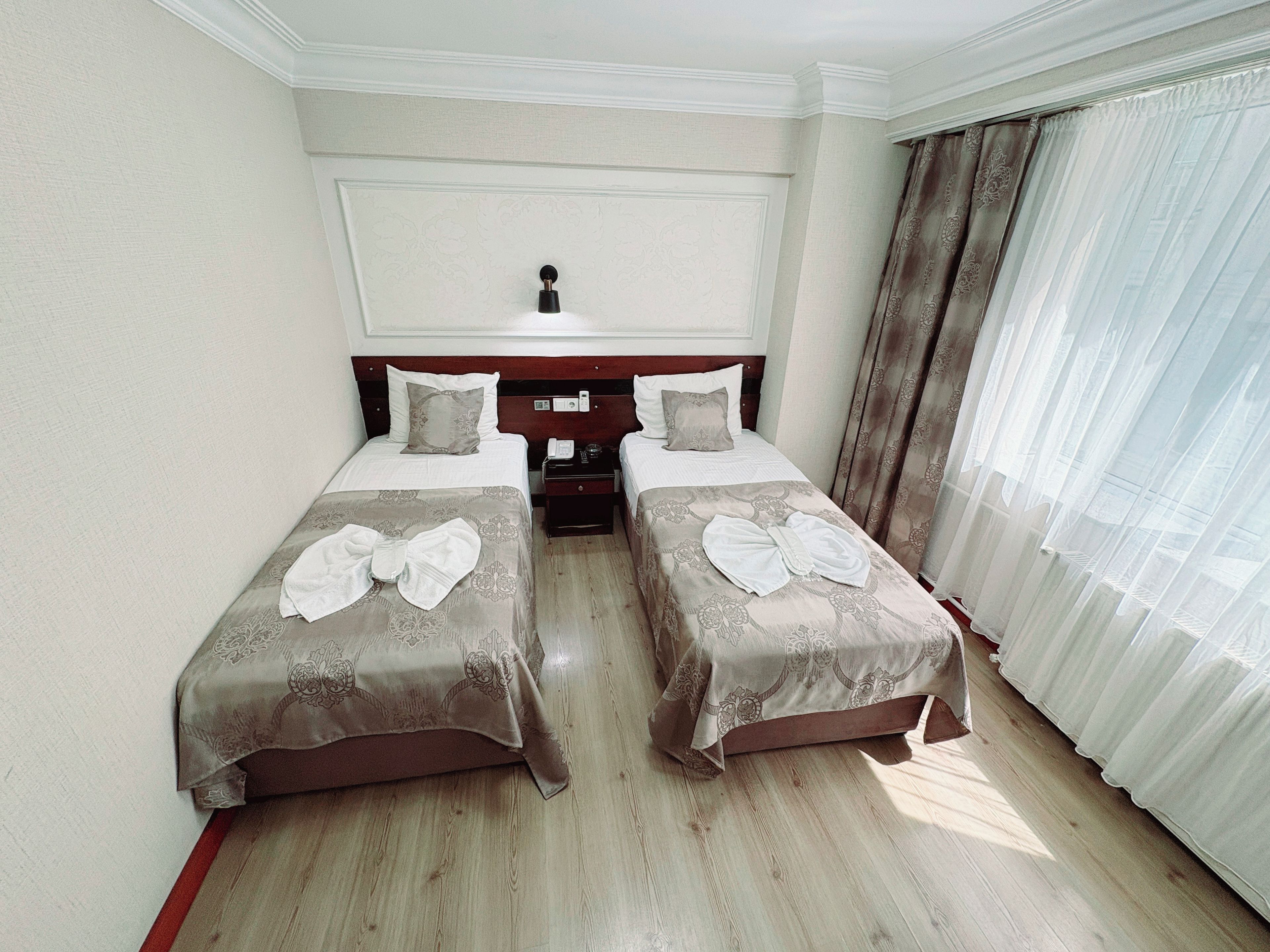 A hotel room with two beds, a bedside table, a telephone, and a window with curtains.