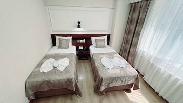 A hotel room with two beds, a bedside table, a telephone, and a window with curtains.