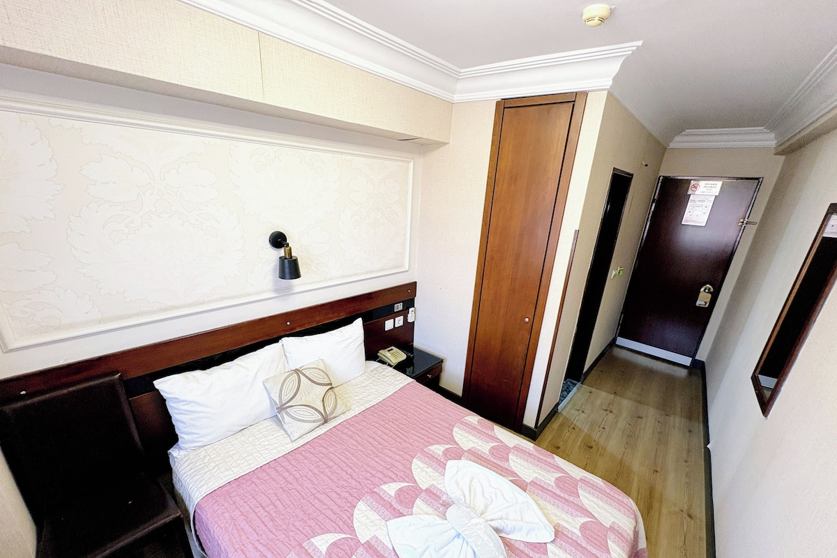 Une chambre d’hôtel avec un lit, une table de chevet, une armoire en bois et une porte.