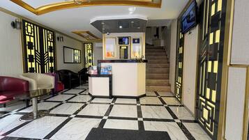 A hotel lobby with a reception desk, seating area, and a staircase.
