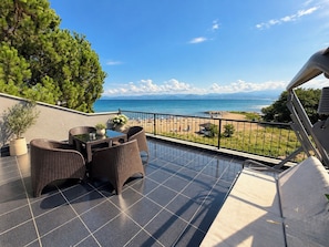 A balcony with a view of the sea, wicker furniture, and potted plants.