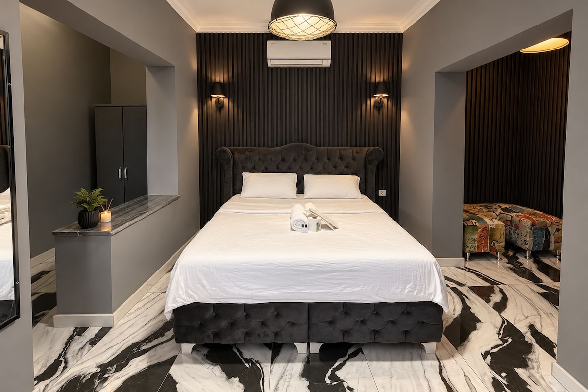 A modern bedroom with a tufted headboard, a marble floor, and a built-in air conditioning unit.