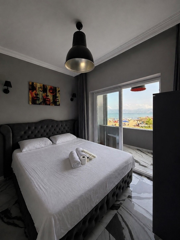 A hotel room with a large bed, a painting on the wall, and a view of the beach.