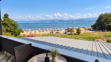 Una terraza con mesa y sillas, con vista a una playa con sombrillas y gente.
