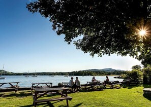 En picknickplats vid sjön med bord och bänkar, båtar på vattnet och en klar himmel.