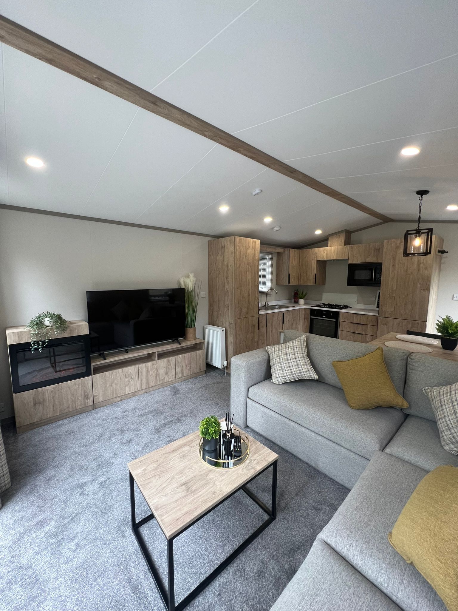 A modern living room with a flat-screen TV, a grey sofa, a coffee table, and a kitchen in the background.