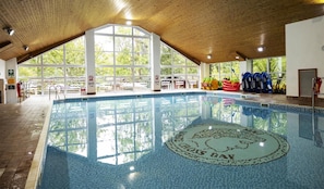 En inomhuspool med fri utsikt över omgivningen, inklusive en vägg med fönster och ett kaklat golv.