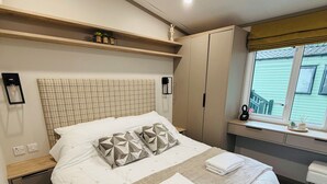 Una cama bien hecha con almohadas y una toalla doblada, una mesita de noche, un armario y una ventana con vistas.