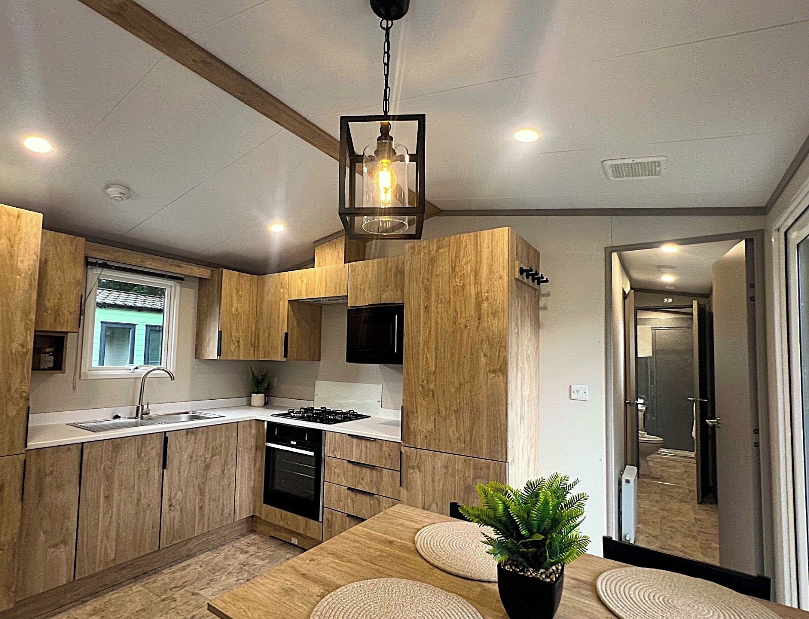 A modern kitchen with wooden cabinets, a built-in oven, a sink, and a dining area with a table and chairs.
