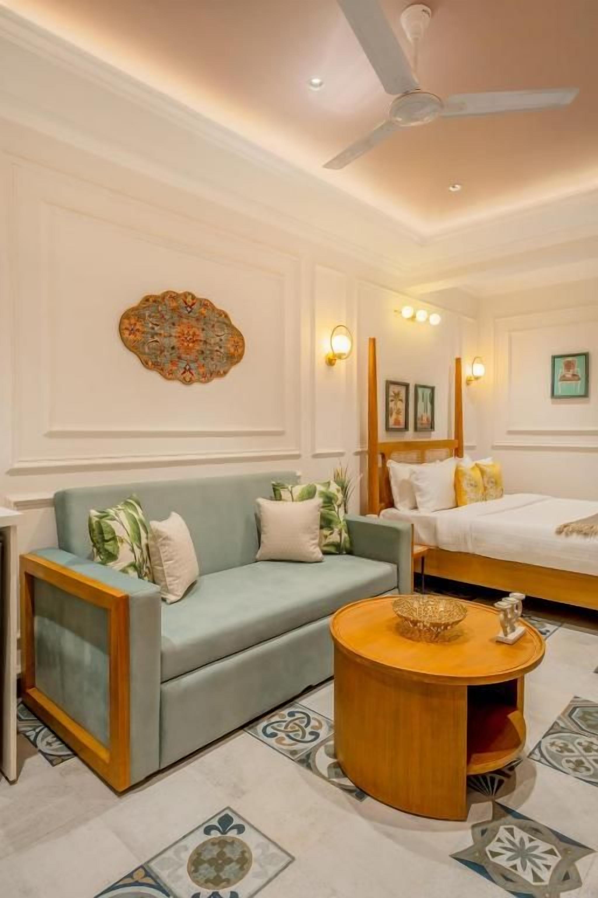 Habitación de hotel con sofá, una mesa redonda de madera, ventilador de techo y cama.