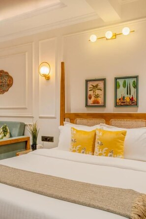 A hotel room with a bed, a nightstand, a lamp, and wall-mounted artwork. - Staymaster Veridian Studio Apt (Goa)