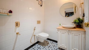 Et badeværelse med hvide flisevægge, et hvidt toilet, et rundt spejl, en vask med bordplade og et bruseområde.