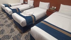 Quarto de hotel com três camas dispostas em linha, um quadro na parede e um tapete estampado.