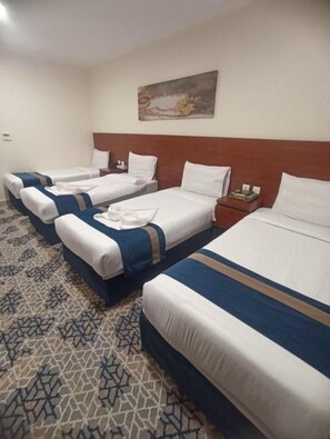 Ein Hotelzimmer mit drei nebeneinanderliegenden Betten, einem Bild an der Wand und einem gemusterten Teppich.