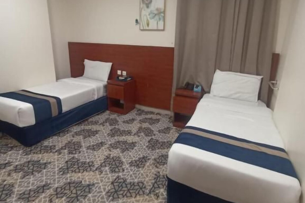Ein Hotelzimmer mit zwei Betten, einem gemusterten Teppich und einem Bild an der Wand.