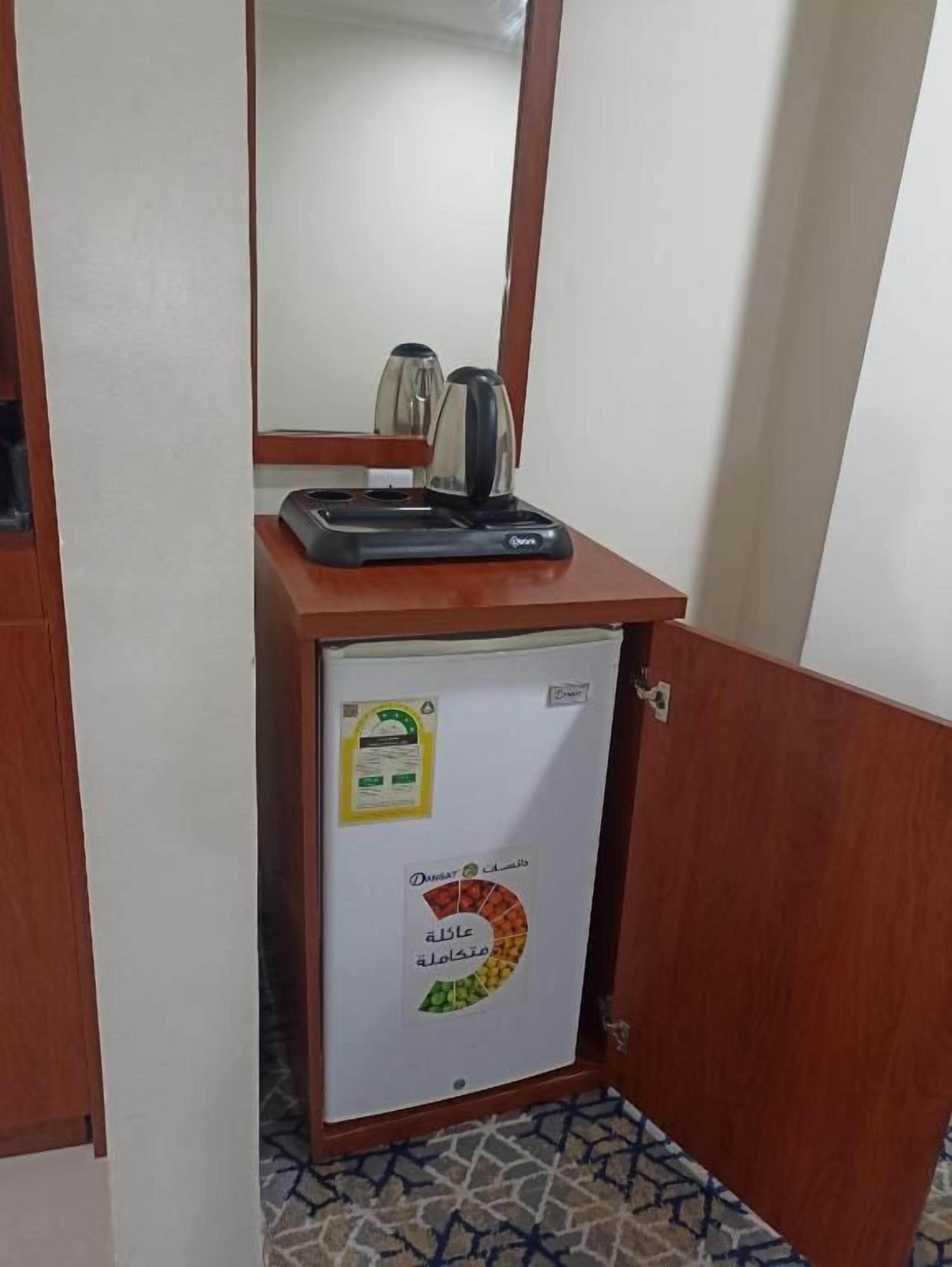 Un refrigerador pequeño con una tetera encima, un espejo arriba y una puerta con cerradura.