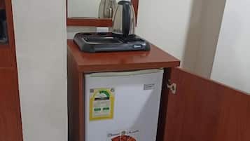 Un refrigerador pequeño con una tetera encima, un espejo arriba y una puerta con cerradura.