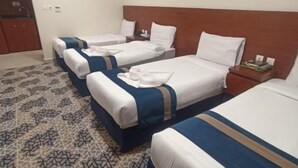 Quarto de hotel com três camas, cabeceira de madeira, tapete estampado e um quadro na parede.