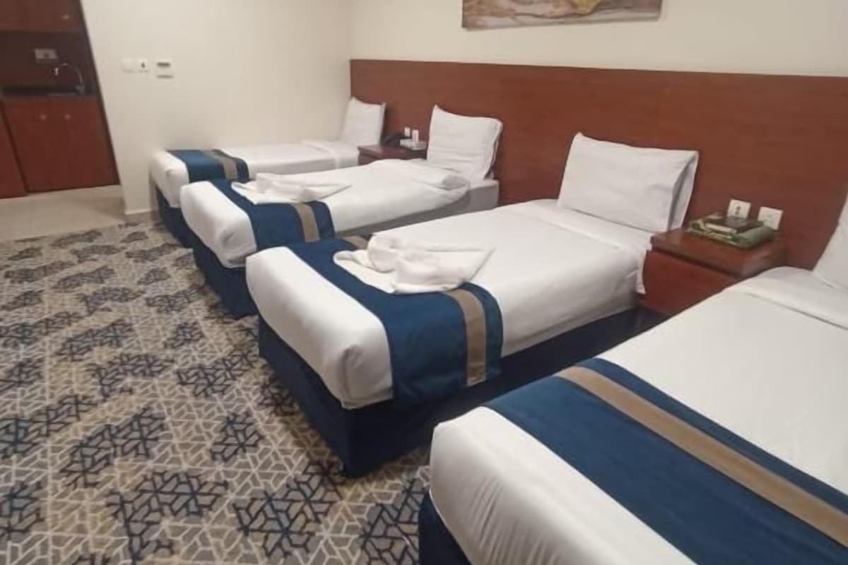 Ein Hotelzimmer mit drei Betten, einem Holzkopfstück, einem gemusterten Teppich und einem Gemälde an der Wand.