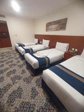 Ein Hotelzimmer mit drei Betten, einem Holzkopfstück, einem gemusterten Teppich und einem Gemälde an der Wand.