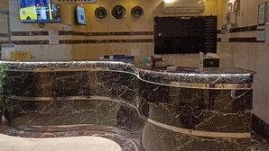 Uma área de recepção com balcão curvo de mármore, mesa de atendimento e televisão fixada na parede.