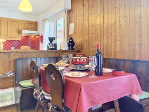 A dining area with a red tablecloth, wooden chairs, a wine bottle, and a coffee machine. - Grand-Pré B by Interhome (Champery)