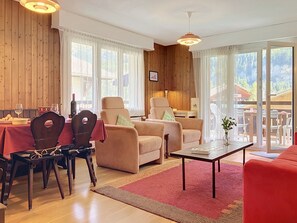 A cozy living room with wooden walls, a dining area with a table set for two, and a view of the outdoors through large windows. - Grand-Pré B by Interhome (Champery)