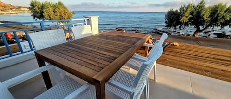 An outdoor seating area with a wooden table and white chairs, overlooking a body of water.
