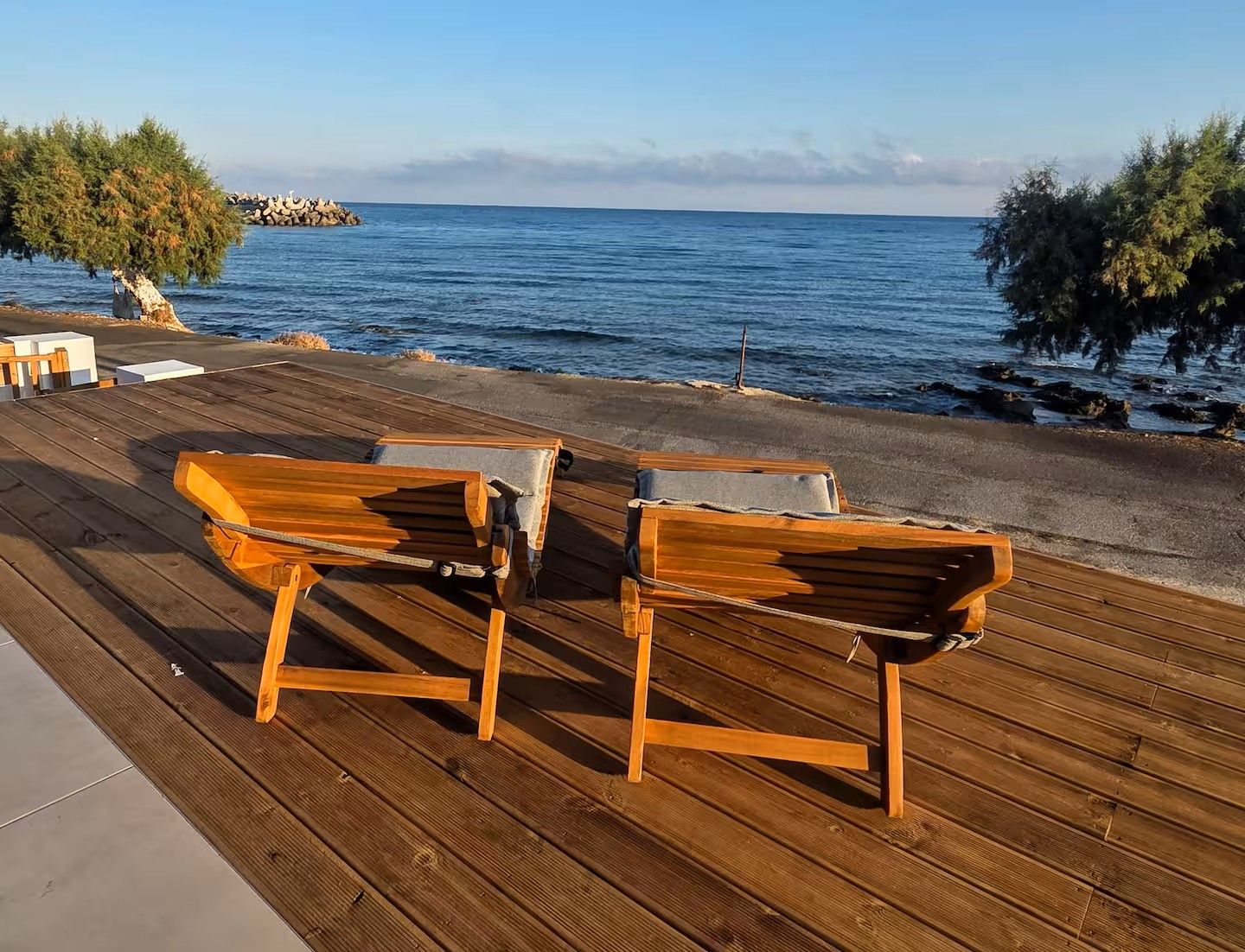 Une terrasse en bois avec deux chaises longues en bois, donnant sur une mer calme.