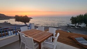 An outdoor seating area with a wooden table and white chairs, overlooking a body of water during sunset. - Arie Waterfront House - A Few Steps to the Sea (milatos beach)