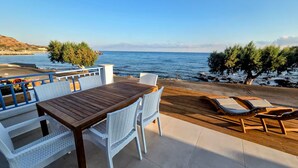 A terrace with a wooden table and white wicker chairs, overlooking a beach and the sea. - Arie Waterfront House - A Few Steps to the Sea (milatos beach)