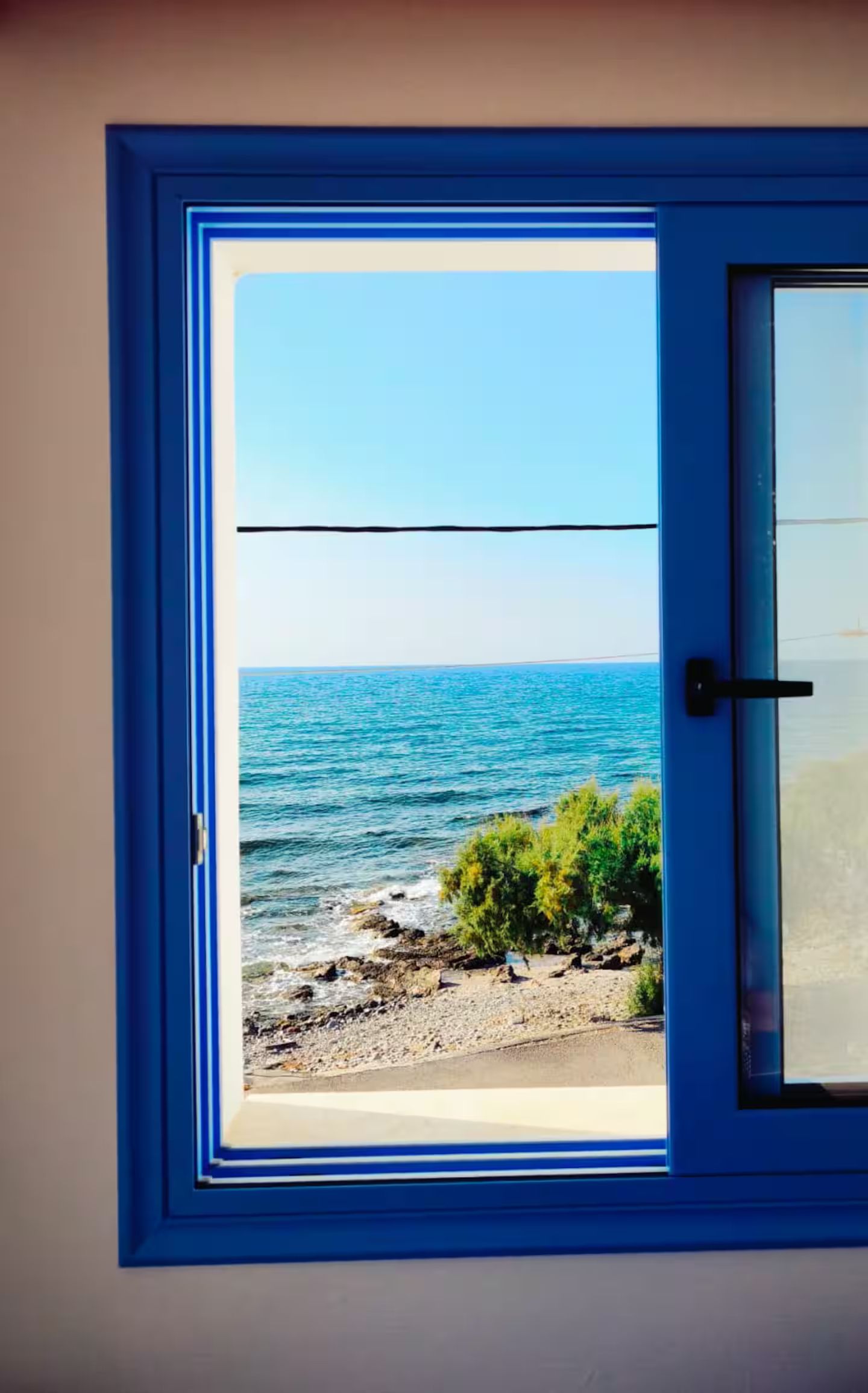Ein Fenster mit Blick auf das Meer und eine felsige Küste.
