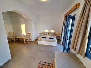 Une chambre d’hôtel avec un lit, deux chaises, une petite table, une fenêtre avec des rideaux et une vue sur l’extérieur.