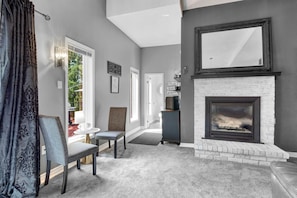 Una sala de estar con chimenea, un comedor con sillas, una mesa de centro y vistas al exterior a través de una ventana.