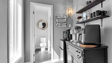 A hallway with a white door leading to a bathroom, a wall-mounted sign reading 'Fresh Brewed Coffee', and a coffee machine on a cabinet.